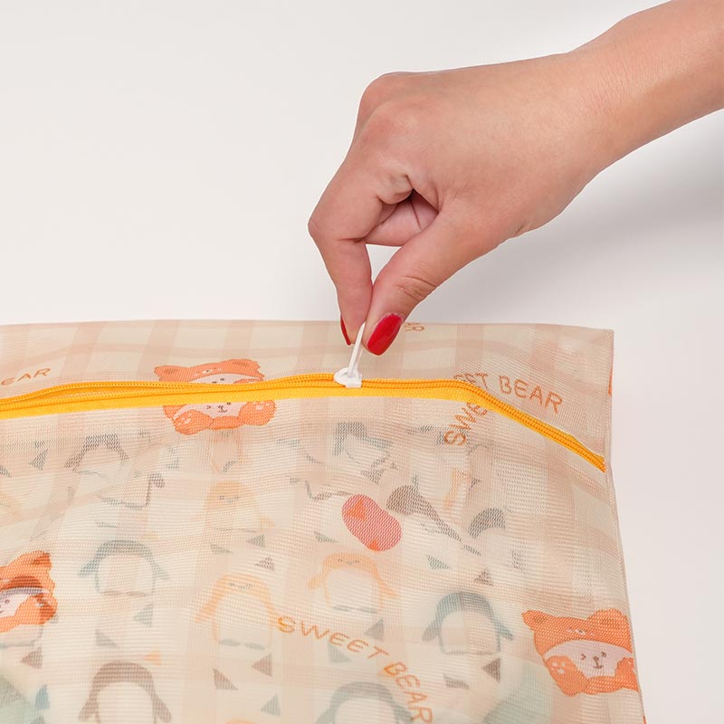 Hand closing the zipper on the mesh CleanPouch Zip Bag, with potty training undies visible in it. 