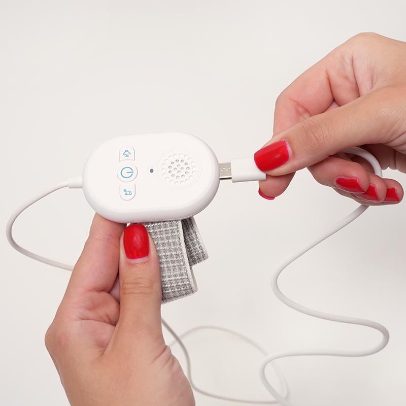 Woman's hand plugging a charging cable into the DreamDry Alarm. 