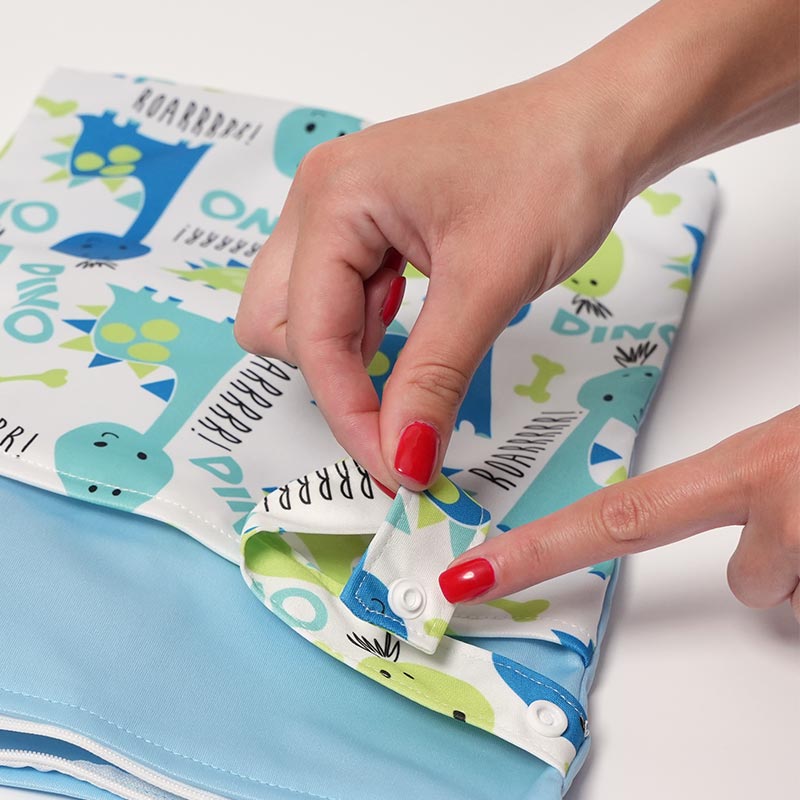 Hands pointing on a button used to safely attach the DuoDry Wet Bag to a stroller, crib, or any bag. 