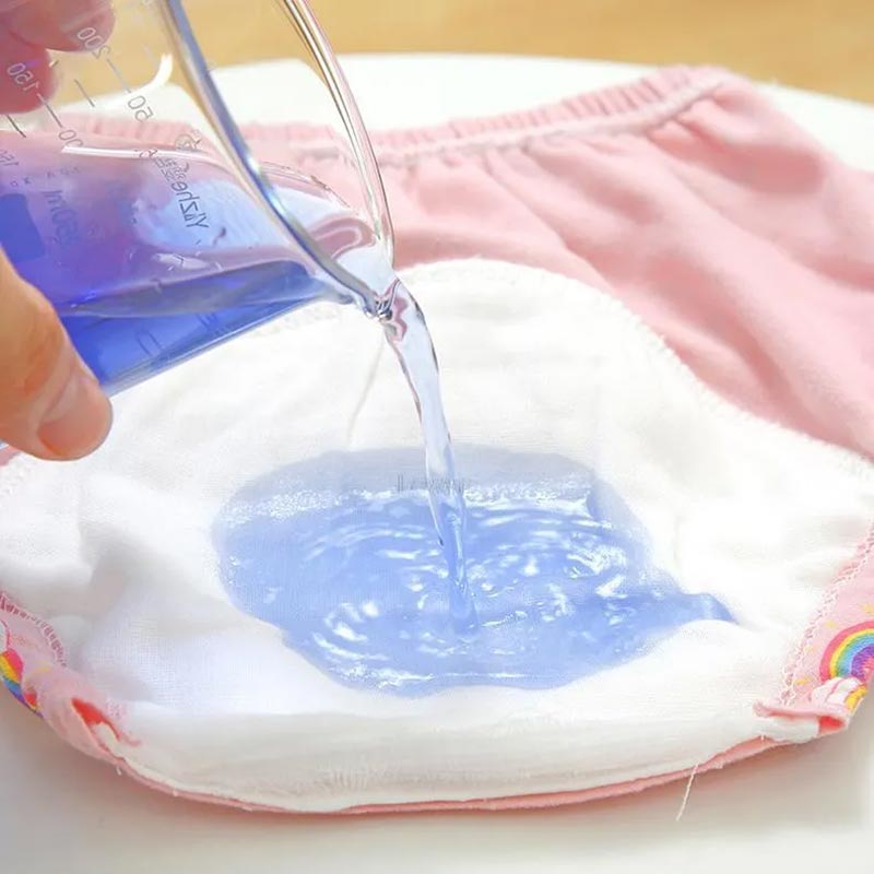 Close up of a blue liquid being poured onto the cotton insert of a Loondie Potty Undies, demonstrating it's leak-proof design. 