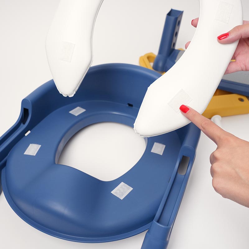 Hands pointing on a Velcro located on the bottom of the cushion that goes onto the Loondie StepUp Seat, a potty training toilet seat for kids.